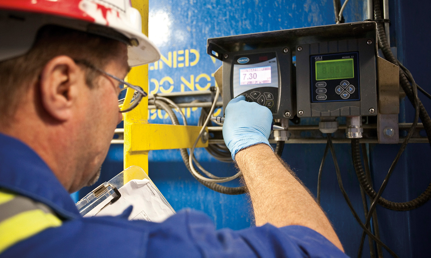 Worker inspecting digital panel with a clipboard in hand